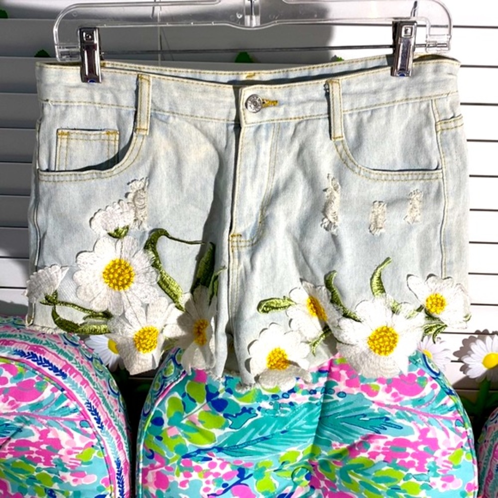 Light gray distressed denim shorts with large daisy appliqué hem in front